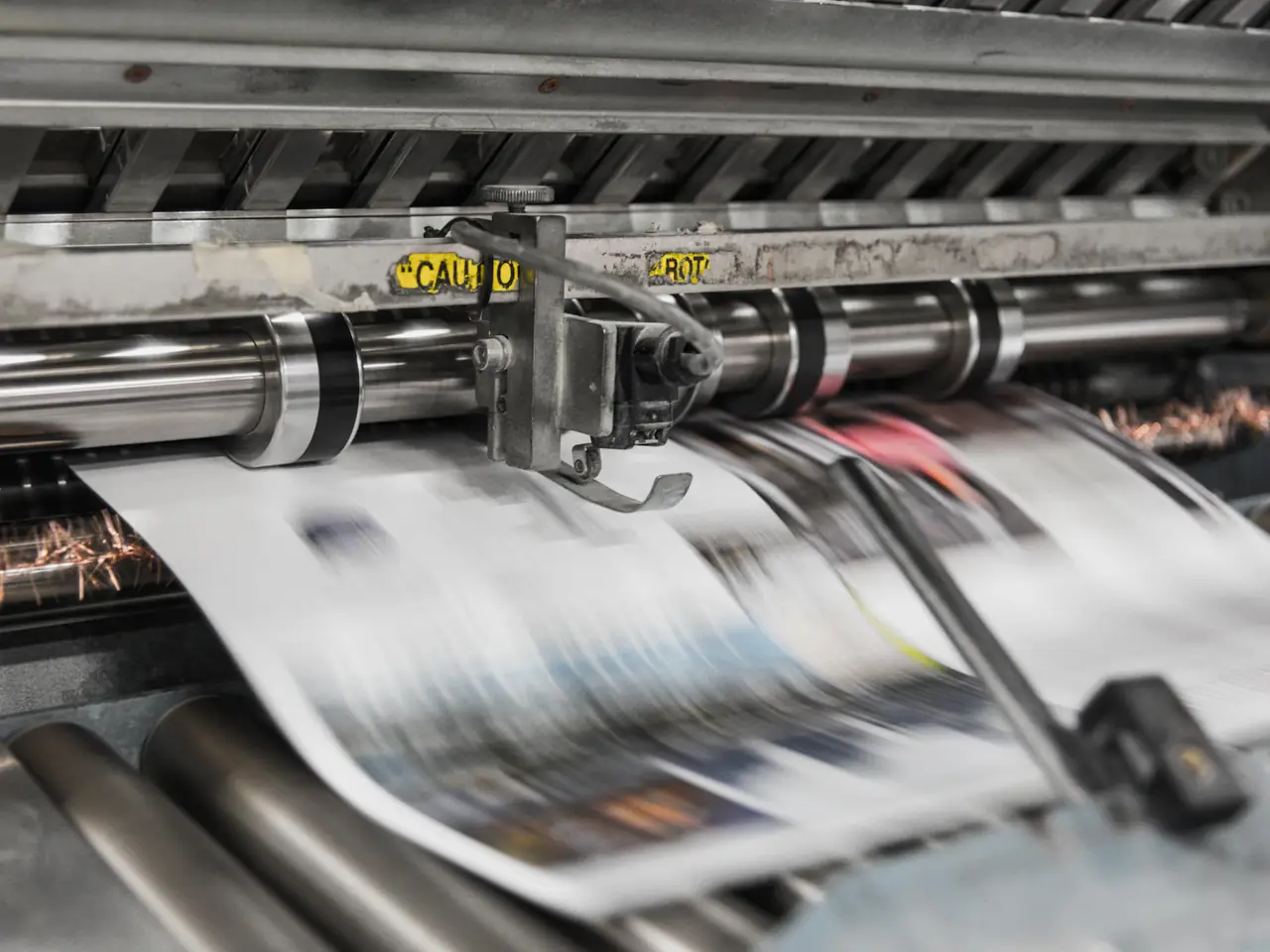 Bedruckte Zeitungsbahnen laufen durch die Walzen einer Rollendruckmaschine in einer Druckerei