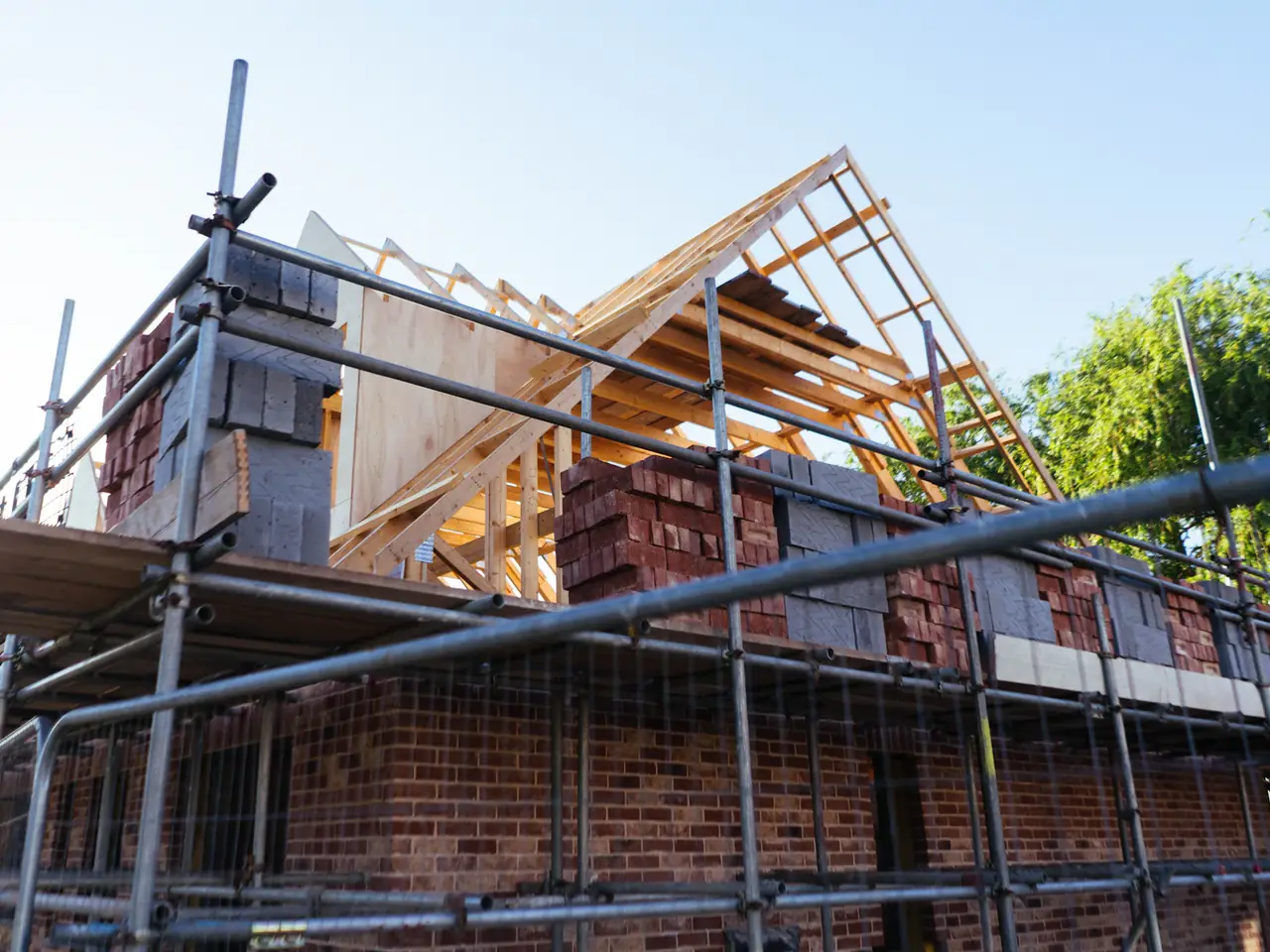 Rohbau eines Einfamilienhauses mit Klinkermauerwerk, Baugerüst und offenem Holzdachstuhl im Sonnenlicht