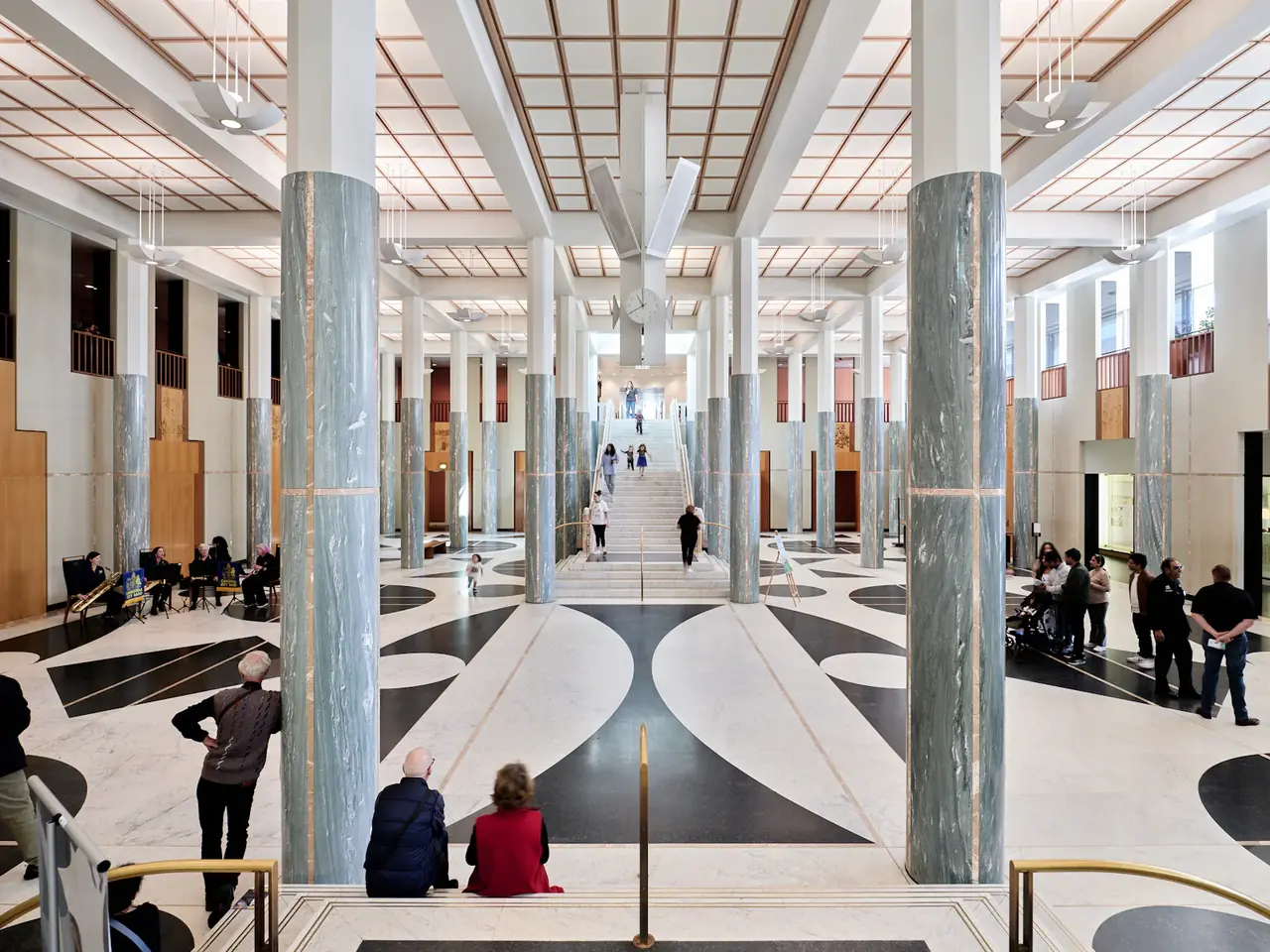 Helles Foyer eines Parlamentsgebäudes mit Marmorsäulen und zentraler Treppe, Besucher gehen durch die Halle