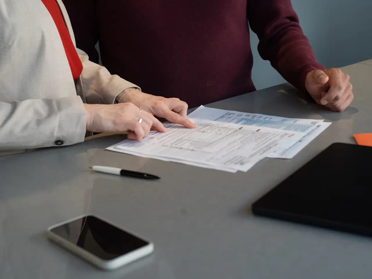 Beraterin zeigt am Besprechungstisch auf eine Zeile in Finanzformularen, ihr Gegenüber hört zu