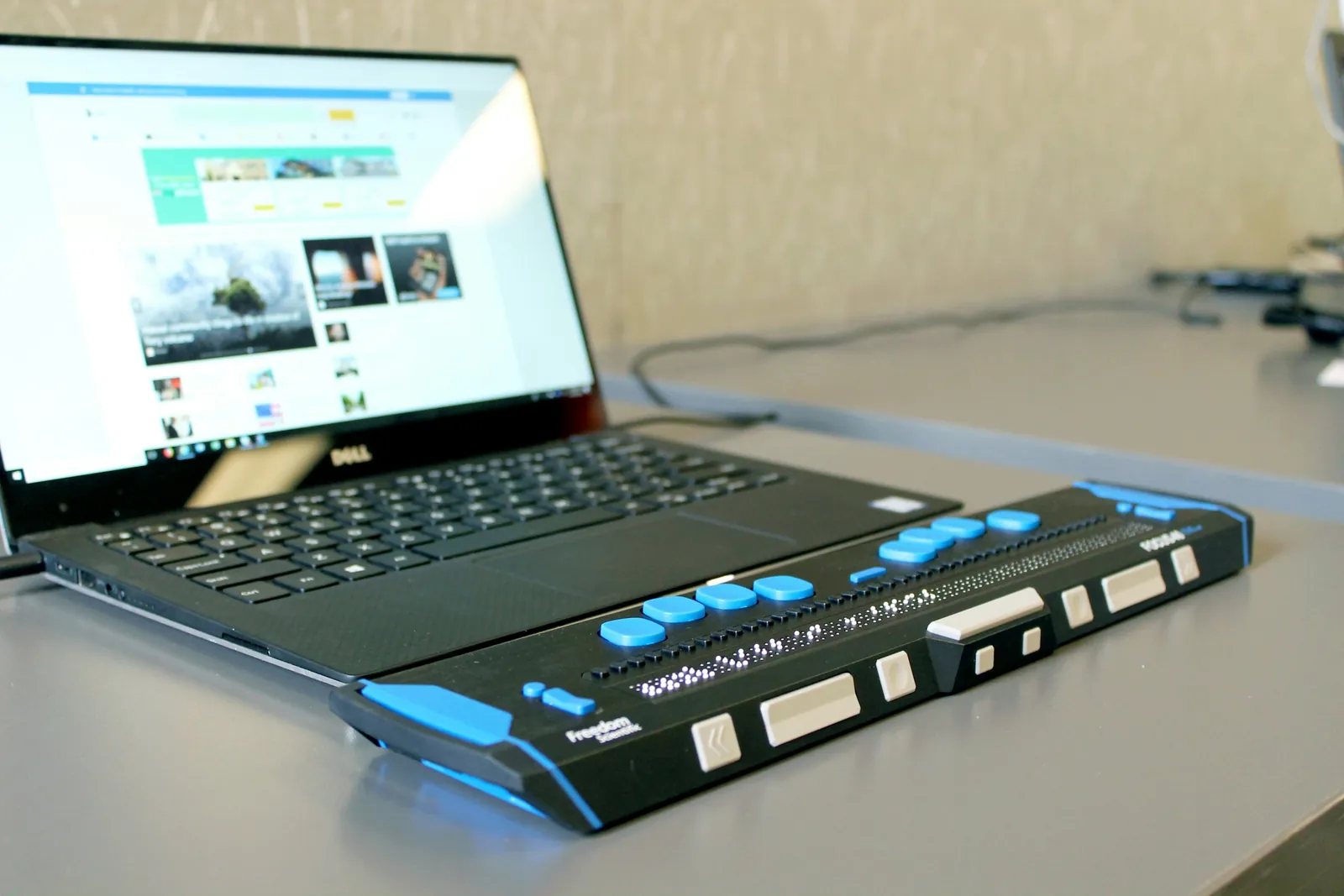 Laptop mit geöffneter Website, davor eine Braillezeile, auf der blinde Menschen den Bildschirminhalt ertasten
