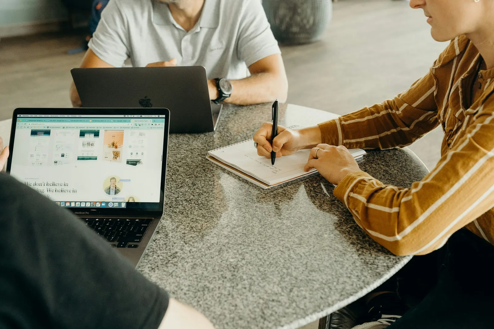 Gespräch am runden Tisch: Eine Person schreibt mit, daneben ist auf einem Laptop eine Website geöffnet