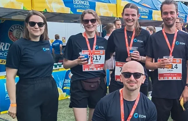 Fünf aus dem Team von EOM in Laufshirts mit Startnummern und Getränken im Stadion nach dem B2Run in Hannover