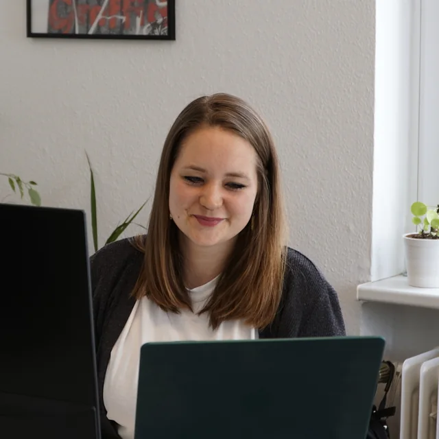 Eine Kollegin von EOM lächelt im Büro hinter ihrem Laptop