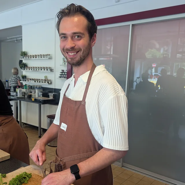Ein Kollege von EOM in Kochschürze schneidet beim Kochkurs Gemüse und lacht