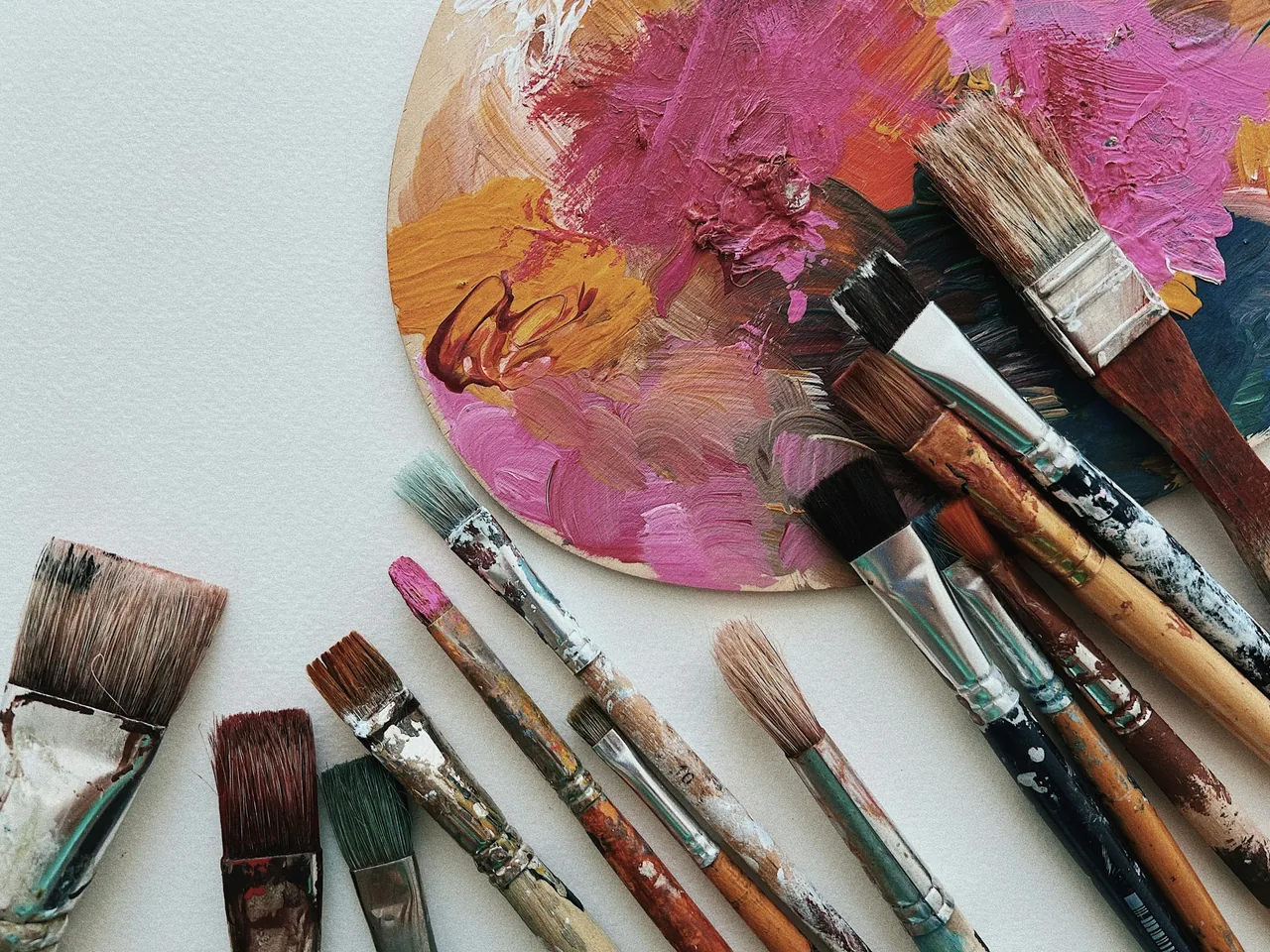 Malpalette mit pinker und orangefarbener Acrylfarbe und benutzten Pinseln auf hellem Papier