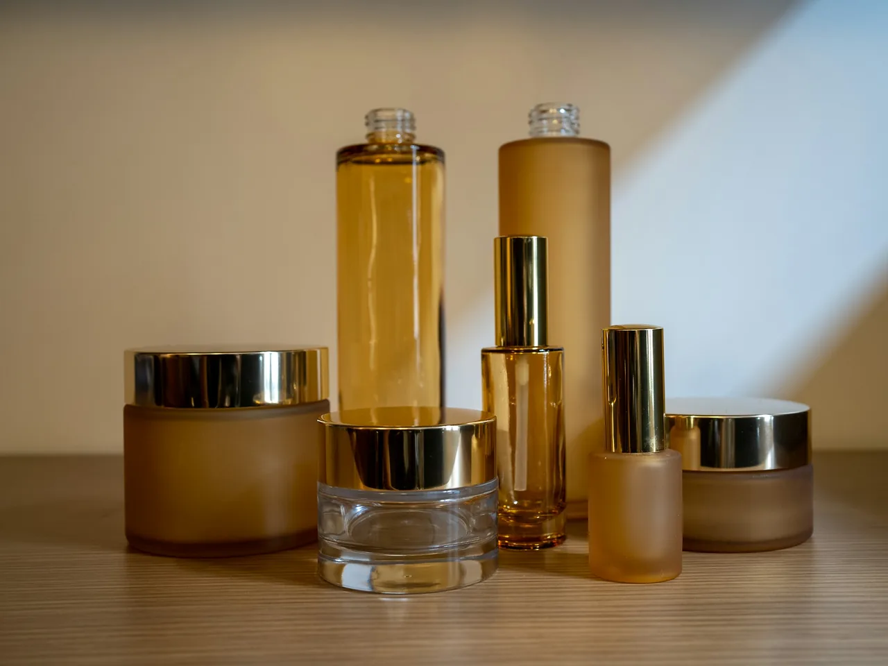 Glastiegel und Flaschen für Pflegeprodukte mit goldenen Deckeln auf einem Holzregal