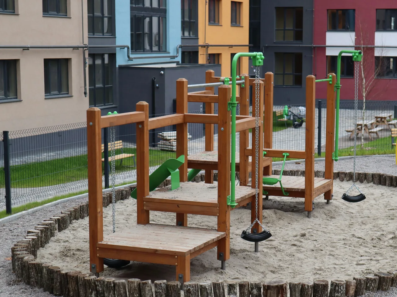 Sandkasten mit Holzpalisade und hölzernem Spielgerät auf einem Spielplatz zwischen Wohnhäusern