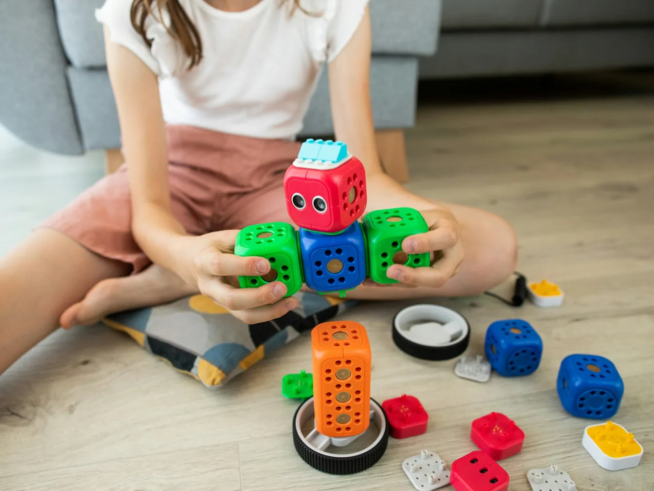 Kind baut auf dem Wohnzimmerboden einen bunten Spielzeugroboter aus Würfelmodulen zusammen