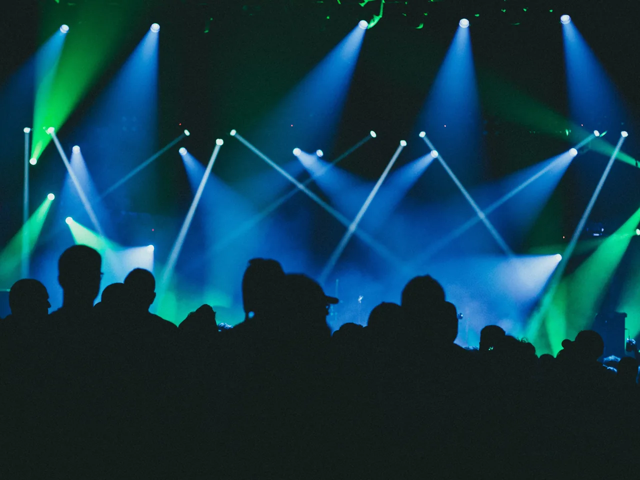 Publikum als Silhouette vor einer Bühne mit blauen und grünen Lichtstrahlen bei einem Konzert